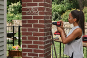 Photo of Craftsman CMCD716 cordless drill used on a brick column outdoors, with tools visible on a nearby table.